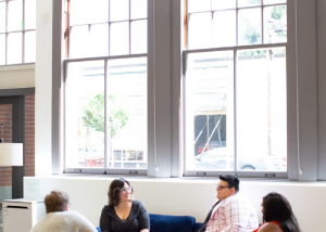 Two people sitting and talking near a large office window